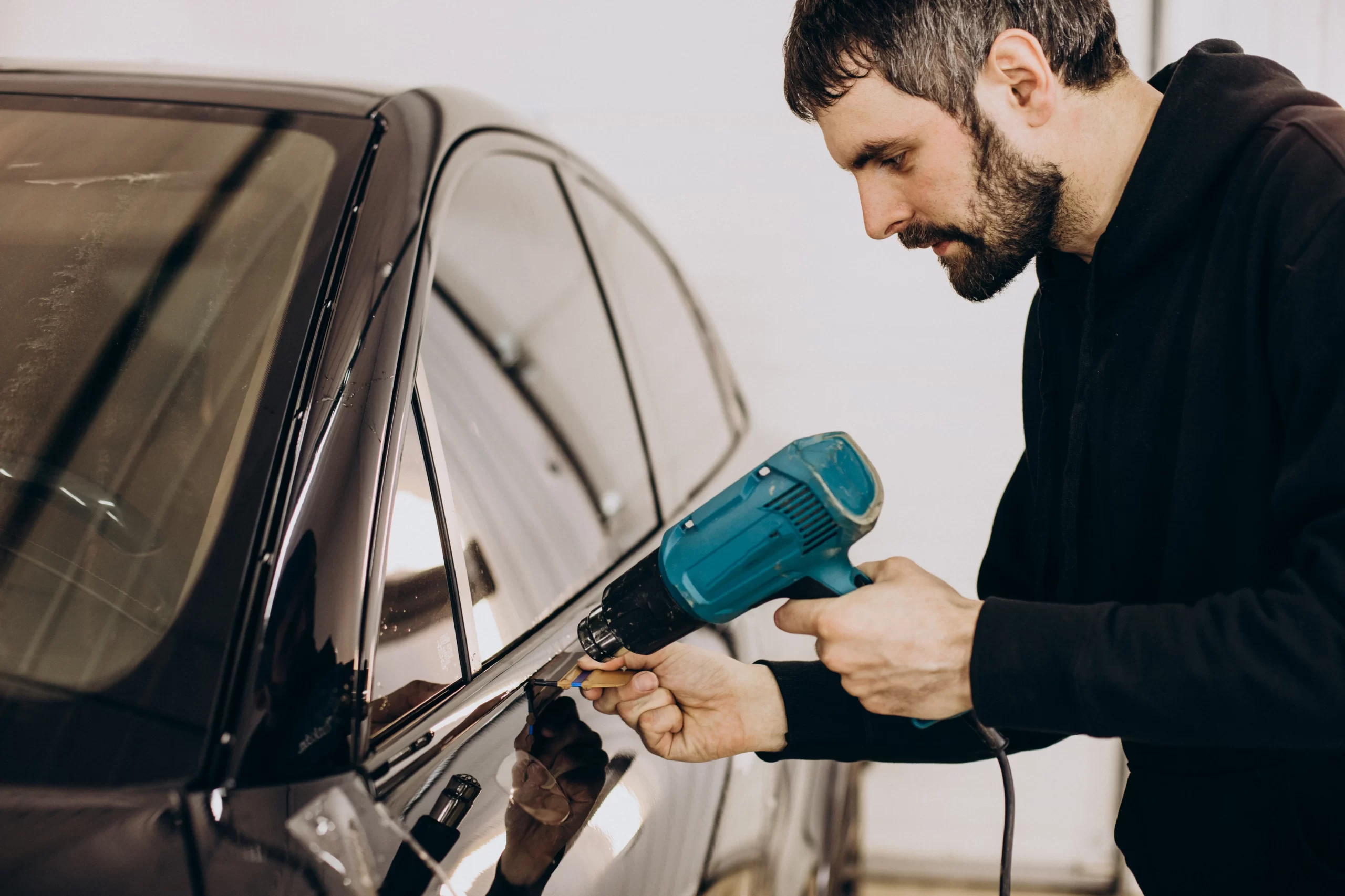 A worker wrapping car window with film.